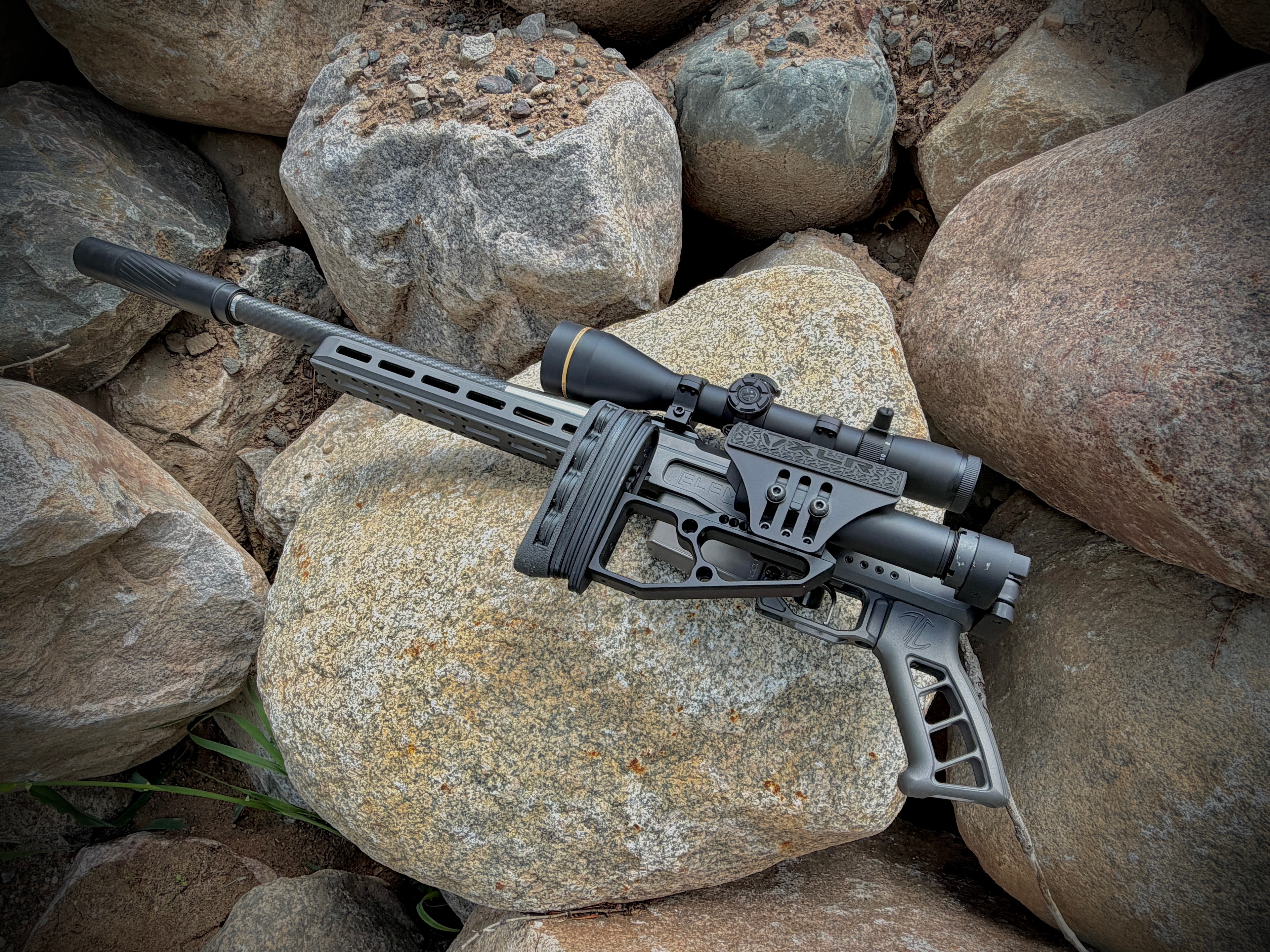 BHE precision bolt-action rifle with carbon fiber suppressor, M-LOK handguard, and Leupold scope resting on granite rocks — custom build by Northwoods Firearms, Crandon, WI