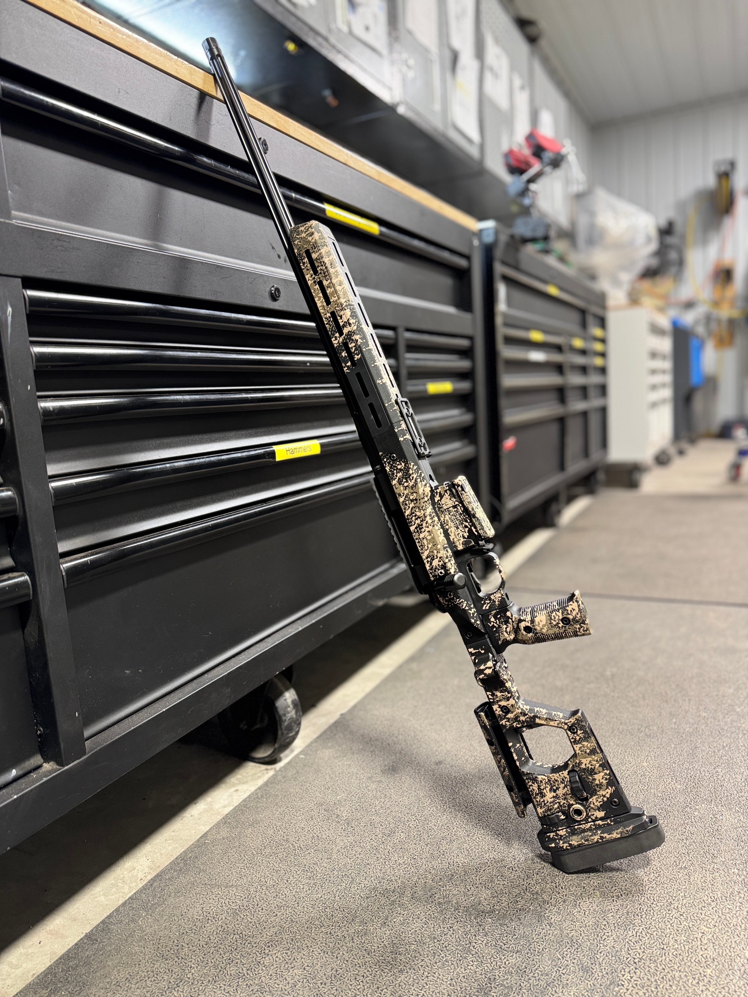 Custom camo precision bolt-action rifle leaning against the Hammerly tool chest in the Northwoods Firearms machine shop, Crandon, WI