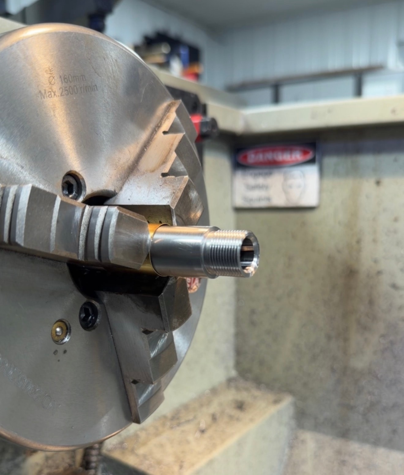 Barrel threading in progress on the lathe at Northwoods Firearms — close-up of threaded muzzle end held in 3-jaw chuck, Crandon, WI
