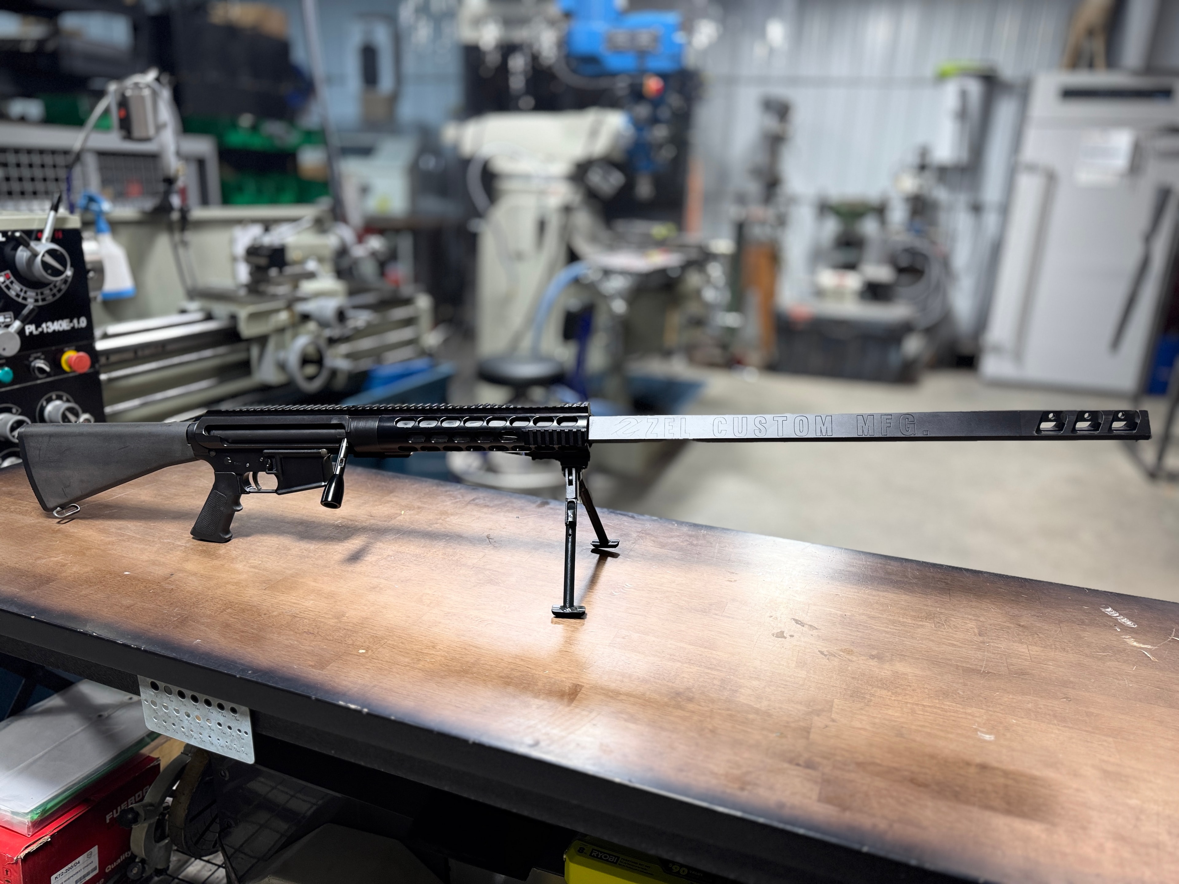 ZEL Custom MFG AR-platform rifle with long fluted barrel on the workbench at Northwoods Firearms machine shop — lathe and mill visible in background