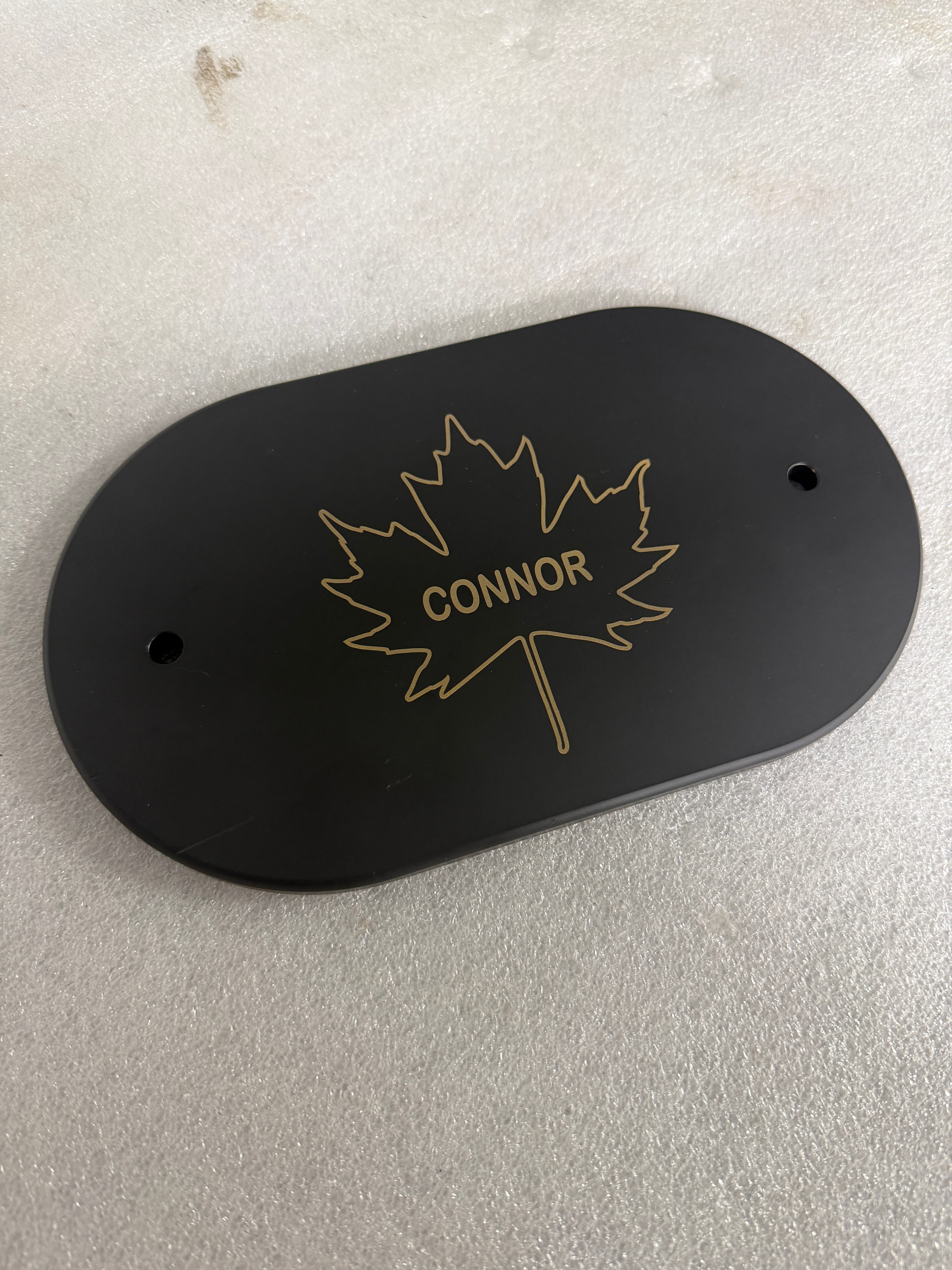 Custom laser-engraved black oval plaque with gold CONNOR text and starburst design by Northwoods Firearms