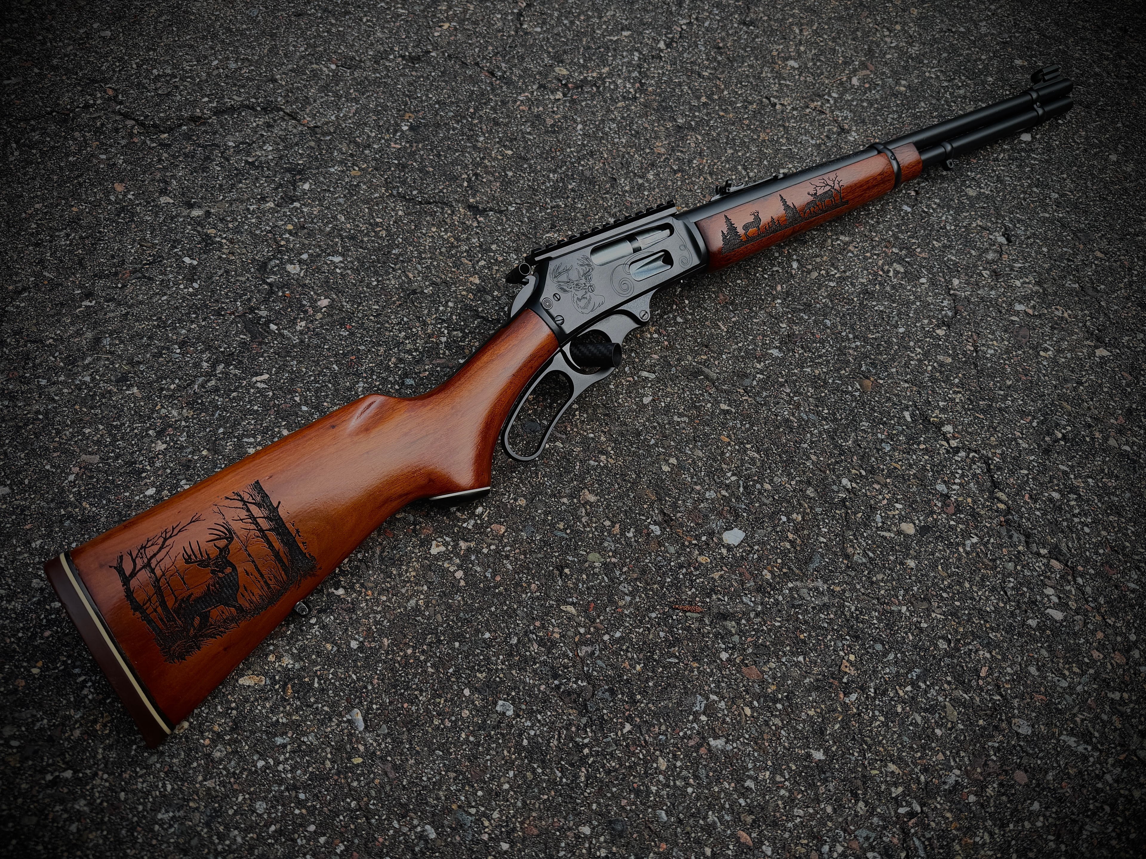 Angled view of laser-engraved Marlin lever-action rifle with whitetail deer and forest scenes on receiver and walnut stock by Northwoods Firearms
