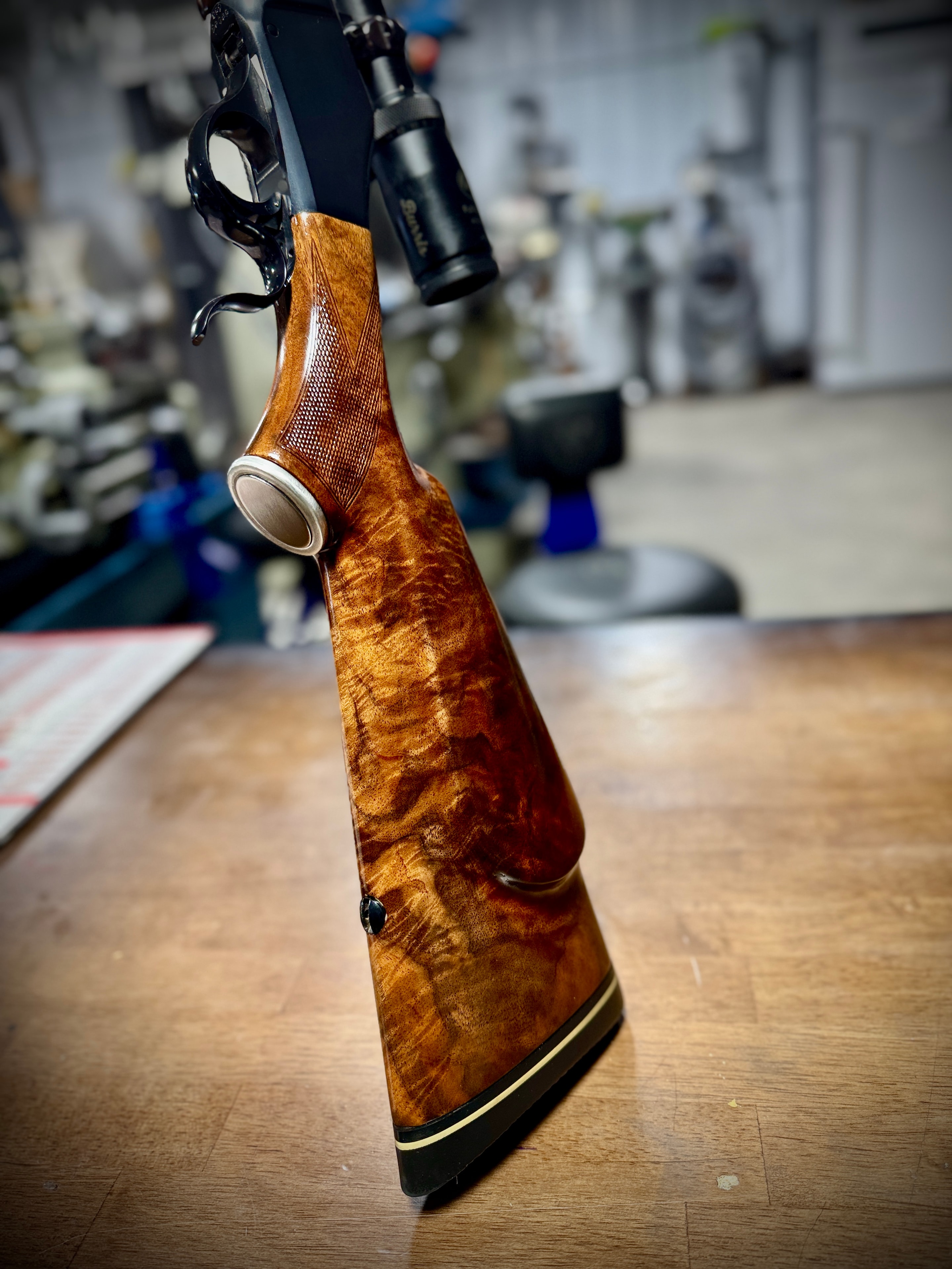 Custom hand-fitted figured walnut rifle stock with hand checkering and ebony grip cap — stock detail standing upright in the Northwoods Firearms shop