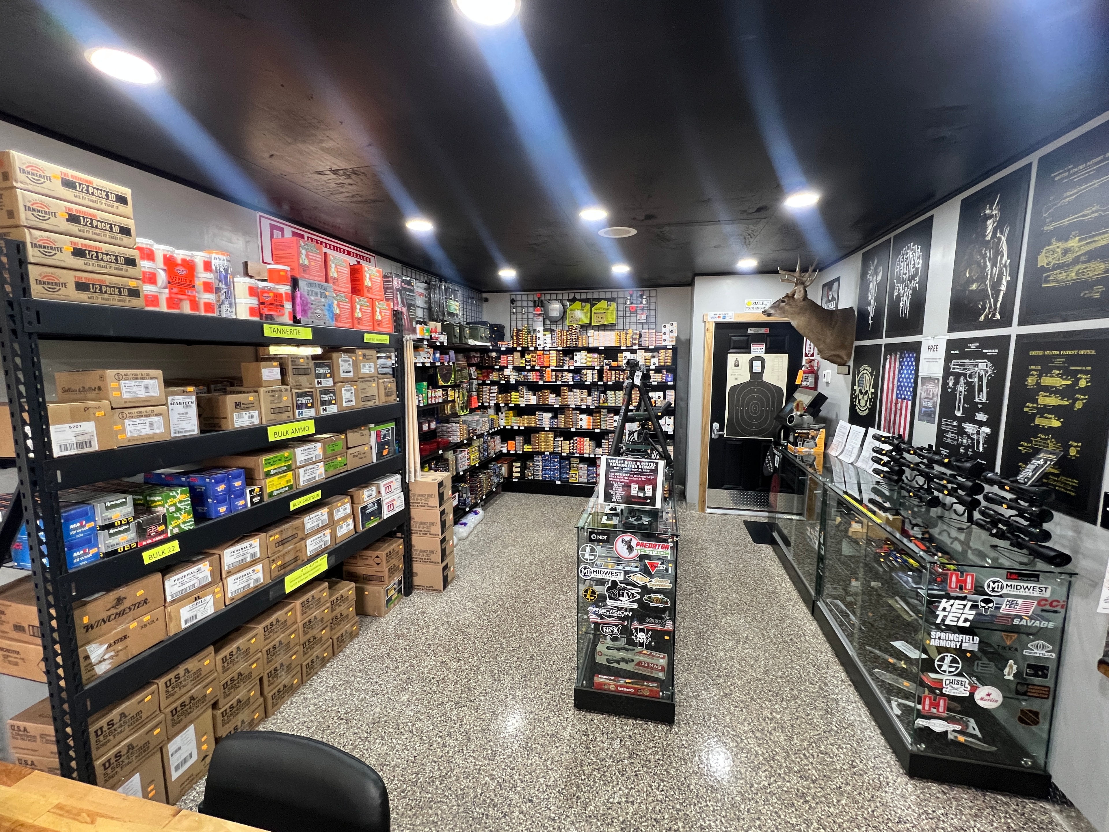 Northwoods Firearms bulk ammo room — Tannerite, Winchester, Federal, and bulk .22 stacked floor to ceiling with scope display cases