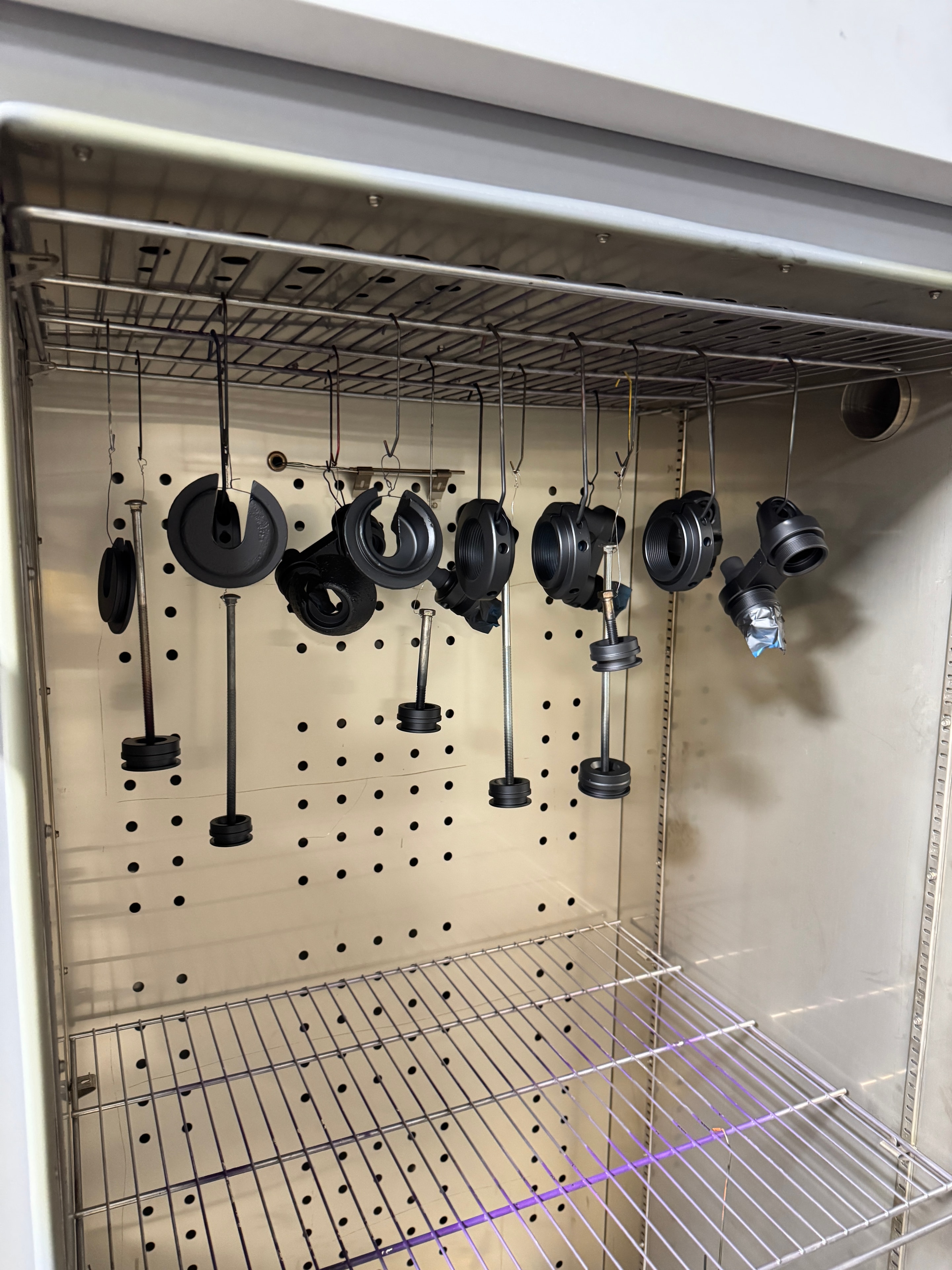 Firearm parts hanging inside the Cerakote curing oven at Northwoods Firearms — suppressor baffles and components ready for coating