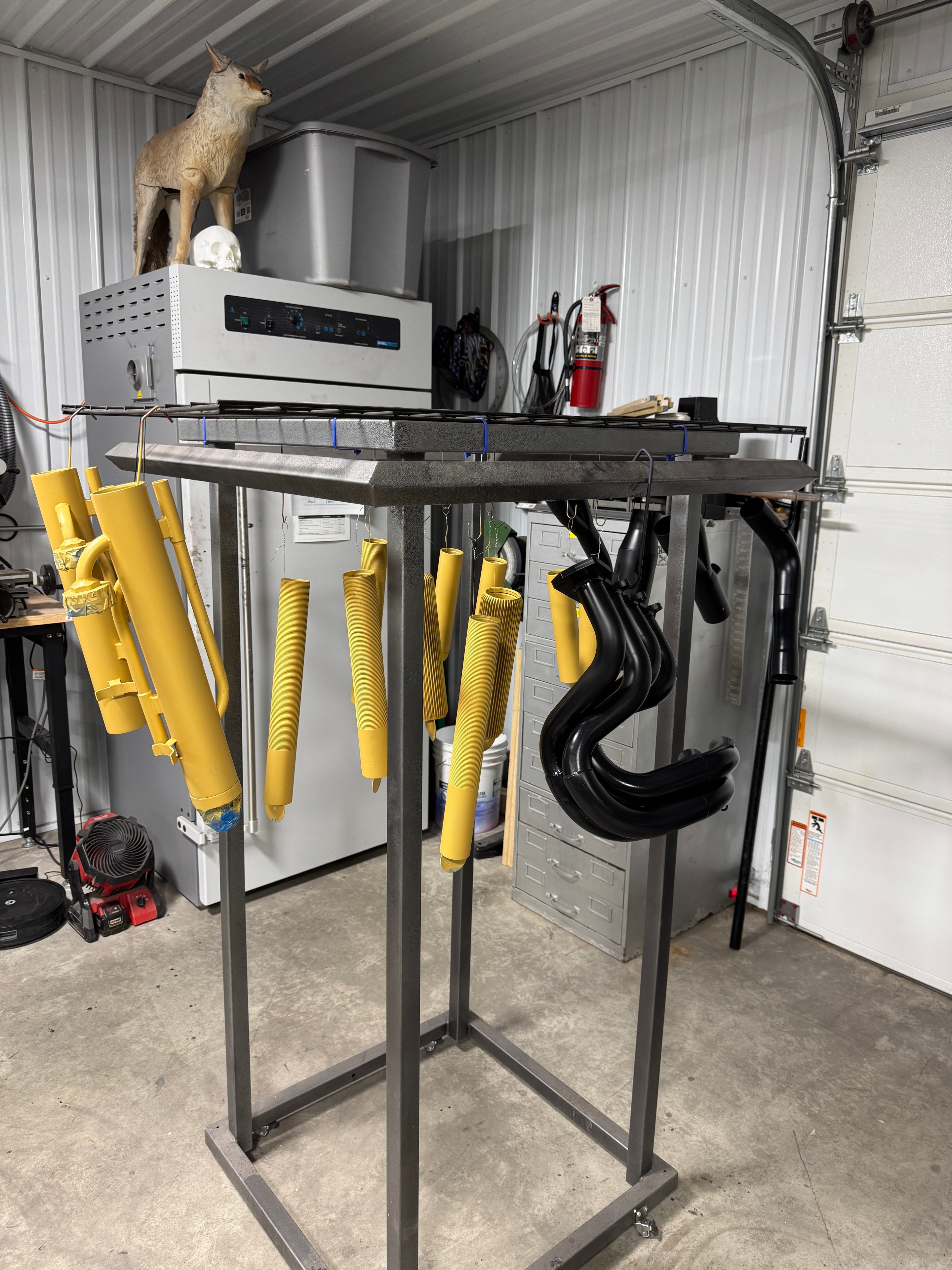Cerakote coating rack at Northwoods Firearms — yellow barrels and black exhaust headers hanging ready for the oven, Cerakote curing oven and media blaster in background