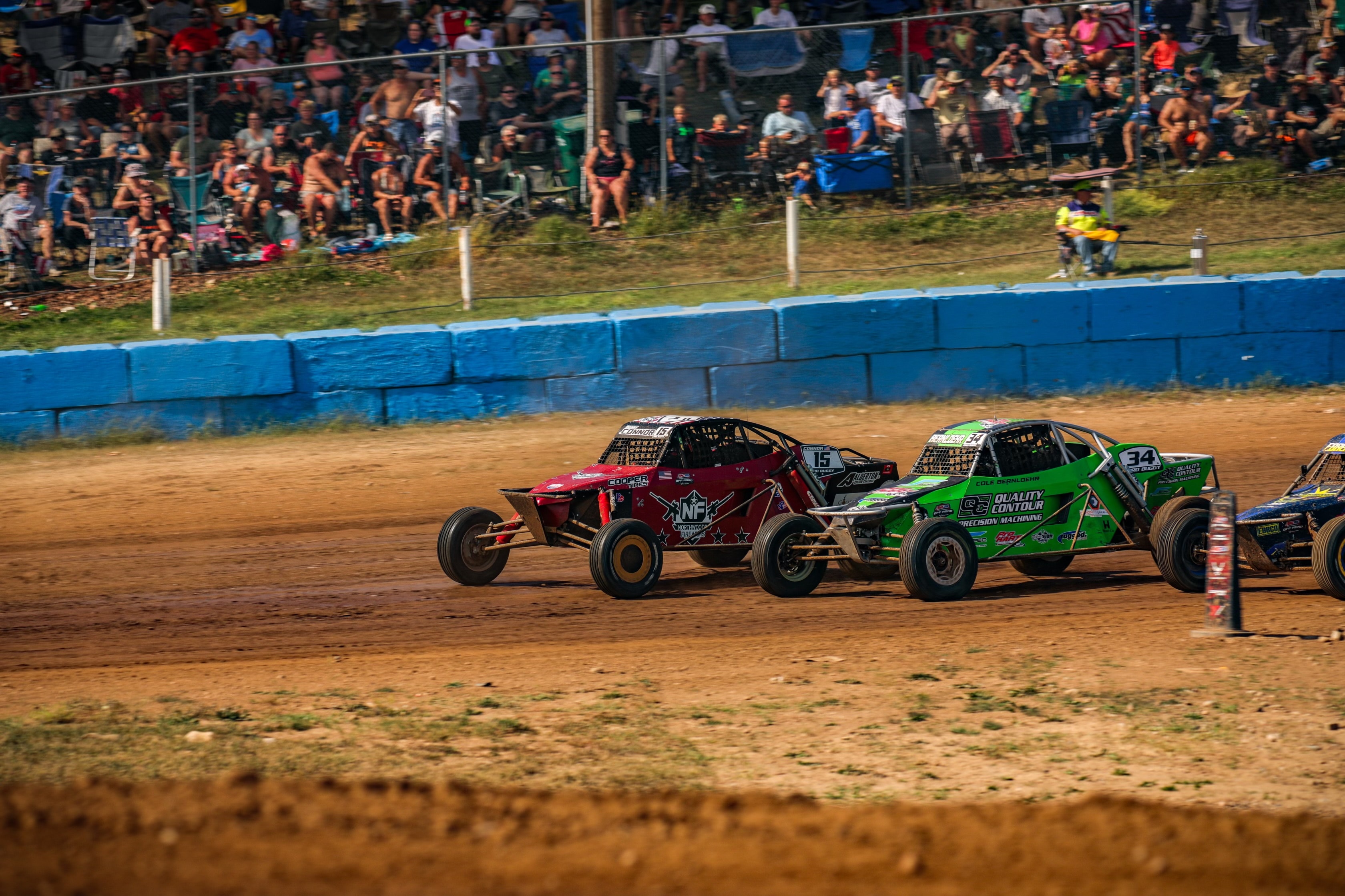 Connor #15 Northwoods Firearms Pro Buggy racing door-to-door with #34 Quality Contour in front of a packed grandstand